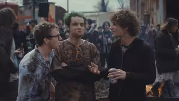 Three mud-covered young men stand close together at an outdoor gathering