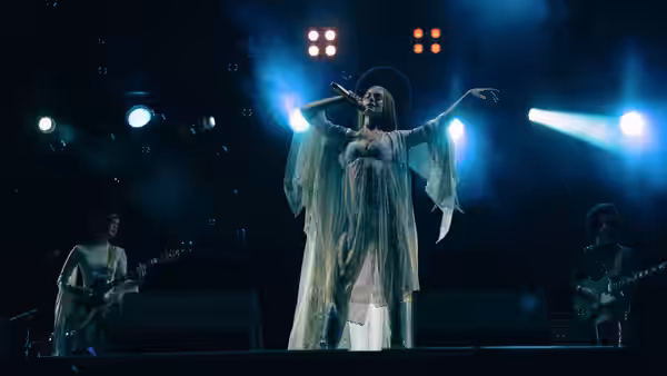 Imogen (FKA twigs) sings on stage with arms outstretched under blue lights