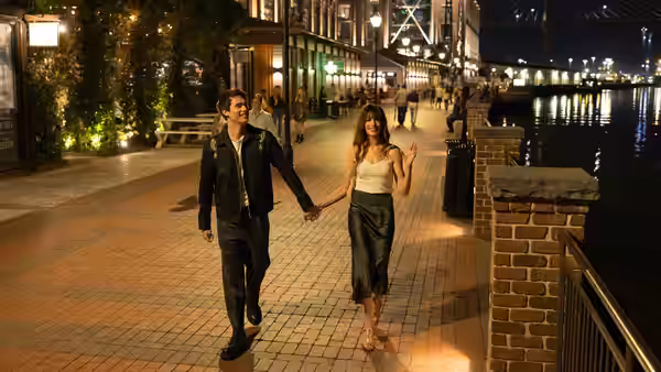 Solène (Anne Hathaway) and Hayes (Nicholas Galitzine) holding hands while walking along a waterfront at night