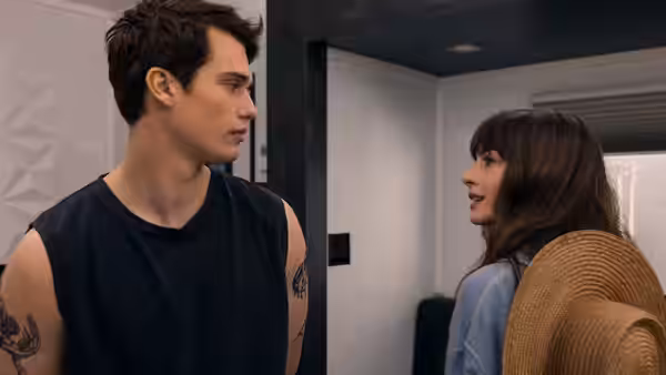 Hayes (Nicholas Galitzine) and Solène (Anne Hathaway) facing each other in a modern indoor hallway