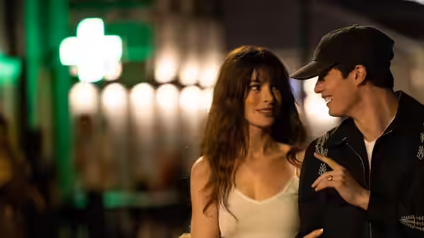 Solène (Anne Hathaway) and Hayes (Nicholas Galitzine) smiling closely together at night with green lights behind them