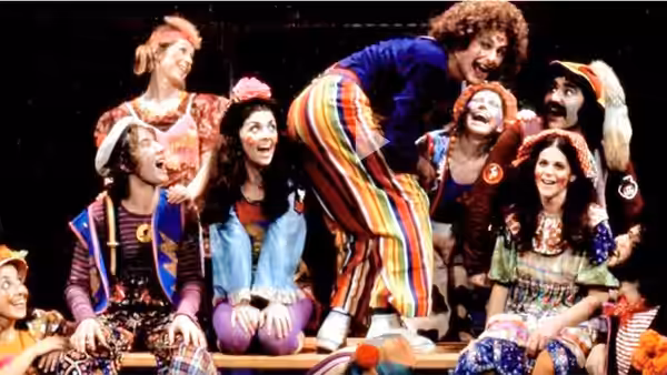 Performers in colorful costumes laugh and lean together on stage