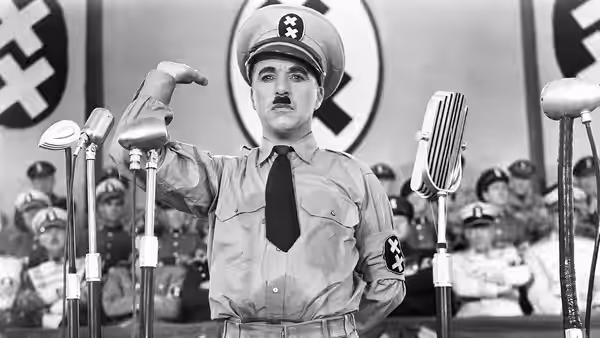 Adenoid Hynkel (Charlie Chaplin) gesturing before microphones at a podium