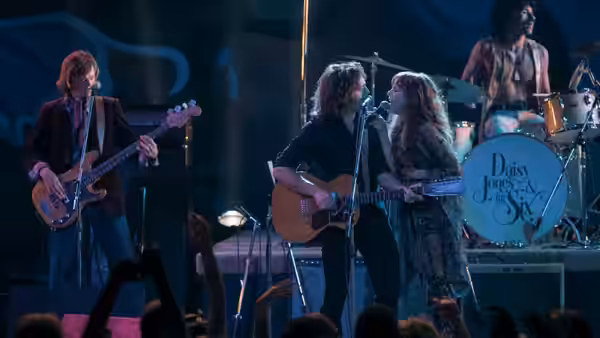 The band performs onstage, with guitarists, singers at microphones and a drummer