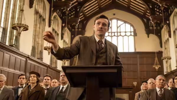 David (Josh O'Connor) addressing an audience from a wooden podium