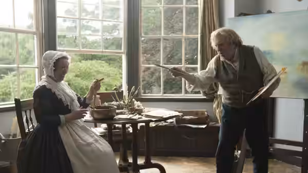 JMW Turner (Timothy Spall) gestures with a brush beside a seated woman in his studio