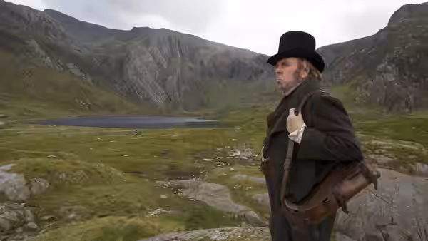 JMW Turner (Timothy Spall) surveys a mountain valley with a sketching bag over his shoulder