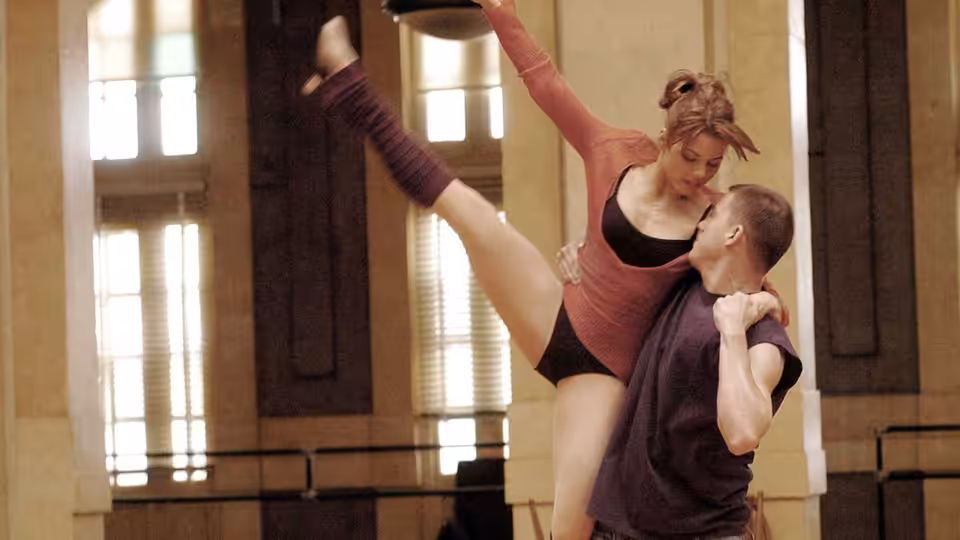 a woman lifts her leg high during a lift in a dance studio
