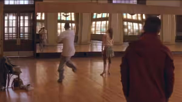 dancers rehearse in a mirrored hall as a man watches from behind