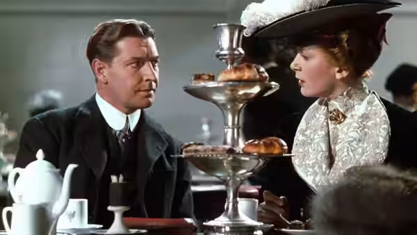 A man and woman talking across a table with pastries and tea