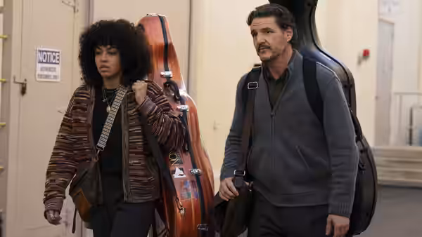 Alex Serian (Pedro Pascal) and a woman carrying instrument cases through a hallway