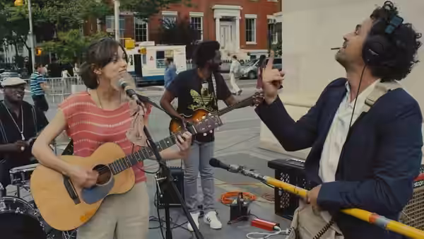 Gretta (Keira Knightley) playing guitar as Dan (Mark Ruffalo) directs on a city street