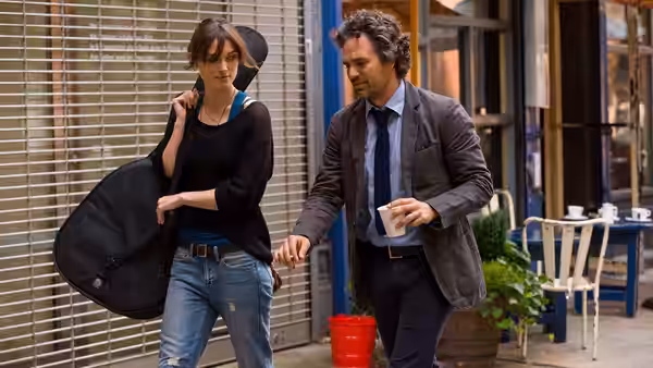 Gretta (Keira Knightley) carrying a guitar case beside Dan (Mark Ruffalo) on a sidewalk