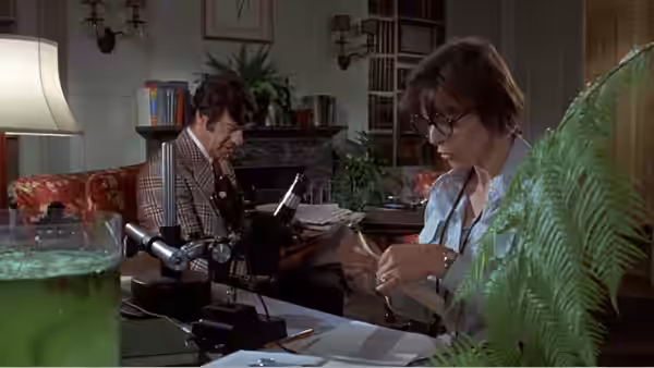 Henrietta Lowell (Elaine May) examines a specimen while a man works at a microscope