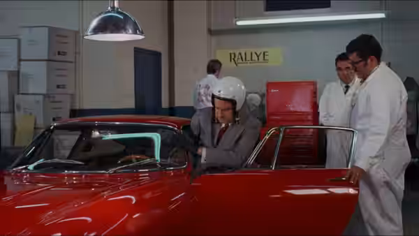 Henry Graham (Walter Matthau) climbs into a red car as mechanics watch in the garage