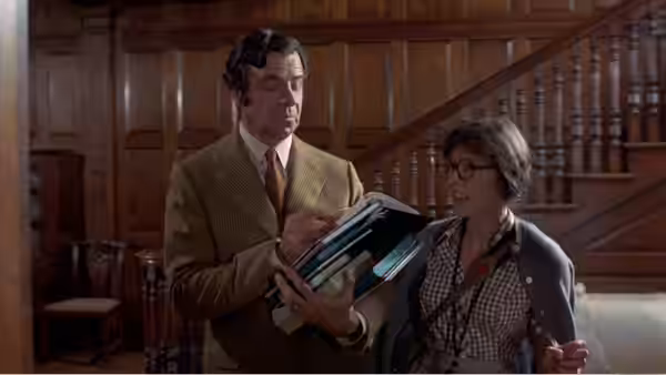 Henry Graham (Walter Matthau) carries books beside Henrietta Lowell (Elaine May) inside a wood-paneled hall