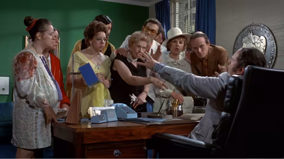 Henry Graham (Walter Matthau) gestures from his desk as a group gathers around him