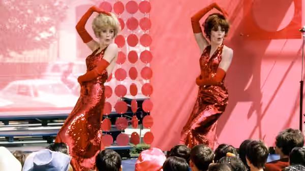 Two dancers in matching red dresses pose before an audience