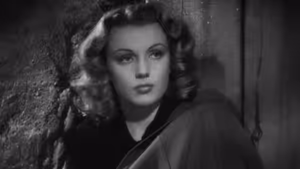 A woman in a dark coat looks over her shoulder indoors