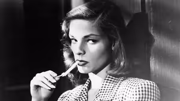 Marie Browning (Lauren Bacall) holds a cigarette holder to her lips