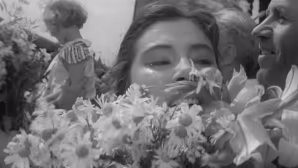 A woman smiles through tears behind flowers as people gather around her