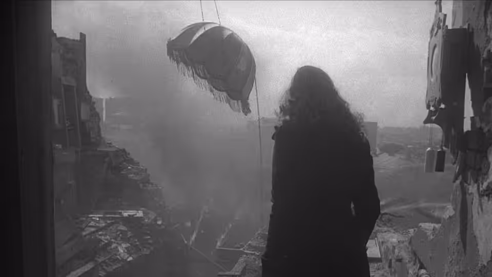 A woman stands silhouetted at a window overlooking a city