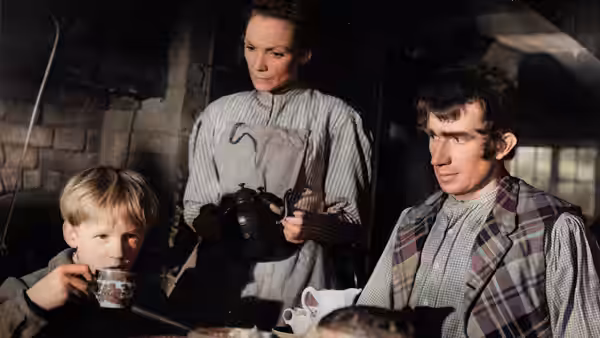 Joe Gargery (Bernard Miles) with a woman and young boy at a table indoors