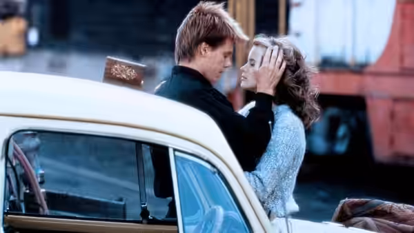 Ren (Kevin Bacon) and Ariel (Lori Singer) sharing a moment beside a vintage car