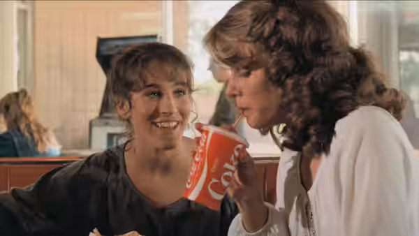 Two young women sharing a Coca-Cola drink at a diner table