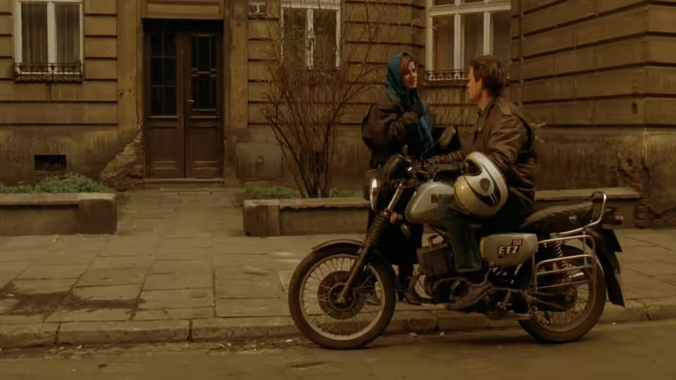 Woman in blue headscarf talking to man on motorcycle outside building