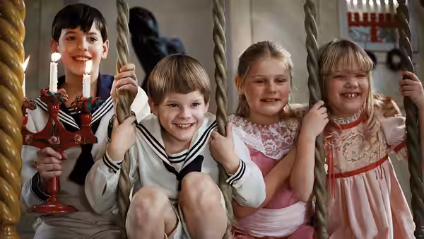 Four children smile while seated on thick ropes holding a candelabra