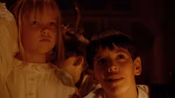 Boy and girl stand side by side in a dimly lit interior looking upward