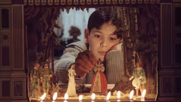 Boy in a knit sweater points at a figure in a candlelit puppet theater