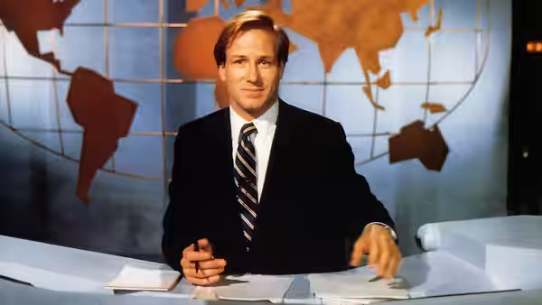 Tom Grunick (William Hurt) seated at the news desk with world map