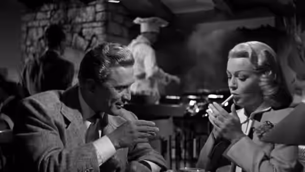 A suited man and a woman smoke together at a table in a restaurant