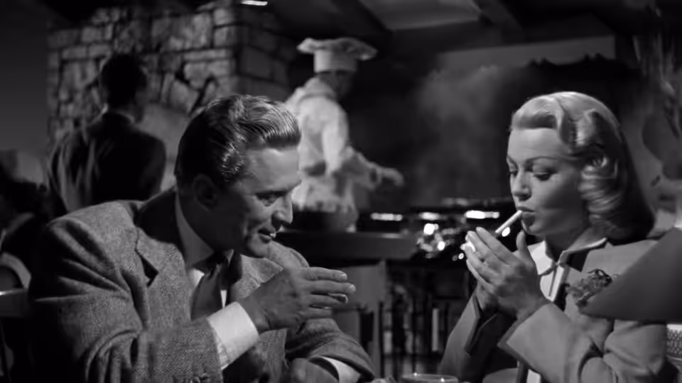 A suited man and a woman smoke together at a table in a restaurant