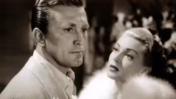 A man in a white jacket looks ahead as a fur-clad woman watches him