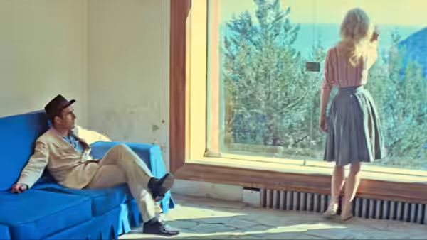 Paul Javal (Michel Piccoli) watches Camille (Brigitte Bardot) standing by a large window