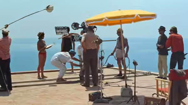 A film crew operates a camera on a seaside terrace
