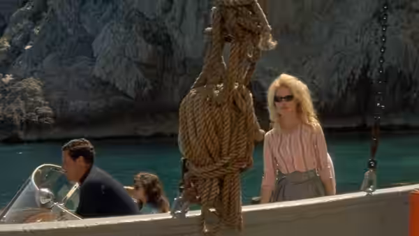 Camille (Brigitte Bardot) stands aboard a boat as men sit near the helm