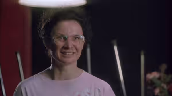 A smiling woman with curly hair and glasses wearing a pink shirt
