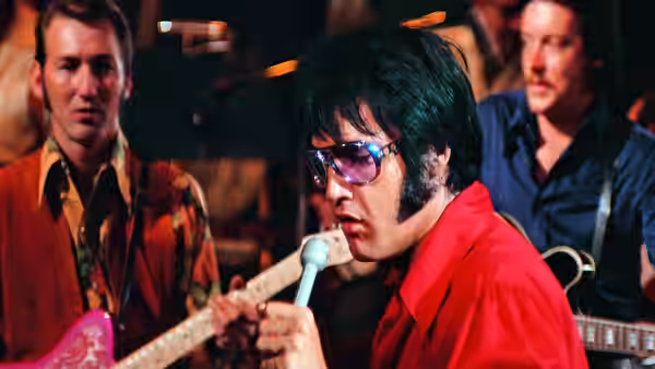 Elvis Presley performing with a guitar and microphone surrounded by band members