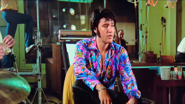 Elvis Presley seated in a recording studio wearing a colorful patterned shirt