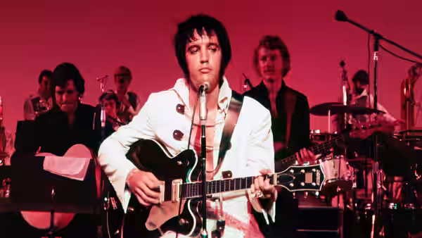 Elvis Presley playing guitar and singing on stage with his band behind him