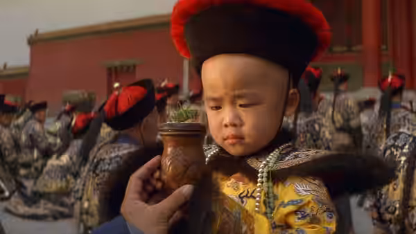 Young boy in yellow imperial robe examines a small plant in a vase held before him