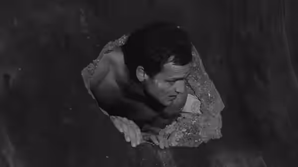 A prisoner climbs through a jagged opening in the floor