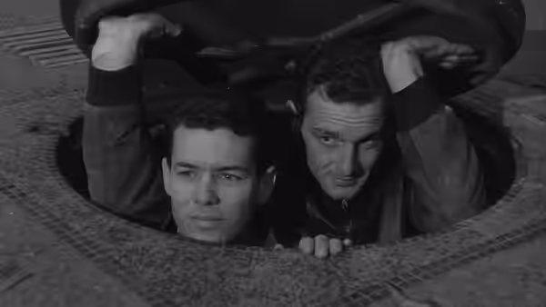Two prisoners peer through a circular opening in the floor