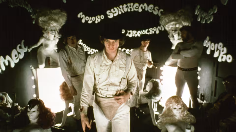 Alex (Malcolm McDowell) walking forward in the Korova Milk Bar among white sculptures