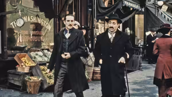 Vito Corleone (Robert De Niro) walking beside a man with a cane on a market street