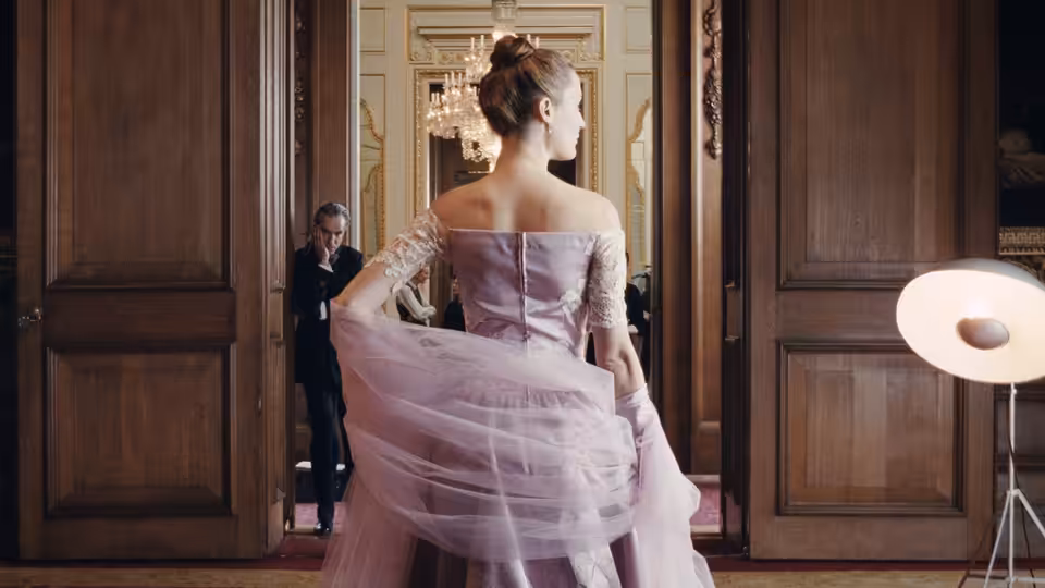 a woman in a pink gown standing in a doorway with a man behind her